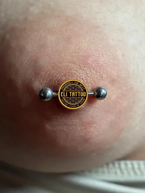Close-up cu un piercing de mamelon realizat cu bijuterie tip barbell drept, cu bile metalice argintii la capete.